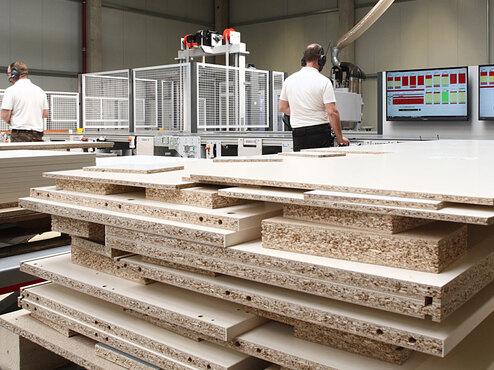 Detailaufnahme von Holzplatten aus CNC Produktion, im Hintergrund Bearbeitung weiterer computergestützter Materialumsetzungen